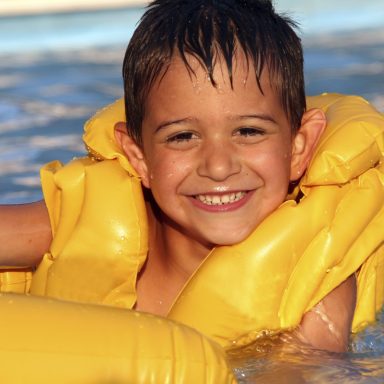 Eine Junge mit Rettungsweste schwimmt fröhlich im Wasser-